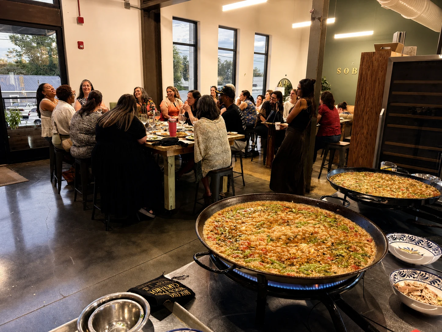 Sobremesa guests gathered around the table while two paellas cook nearby